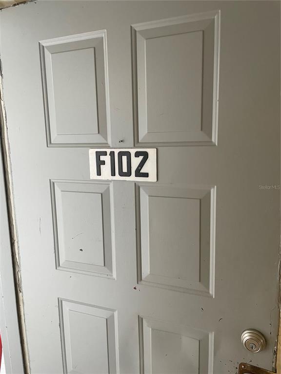 A gray six-panel door features a white sign labeled F102 and a silver doorknob — 584 FAIRWAYS LANE UNIT F102, OCALA, FL