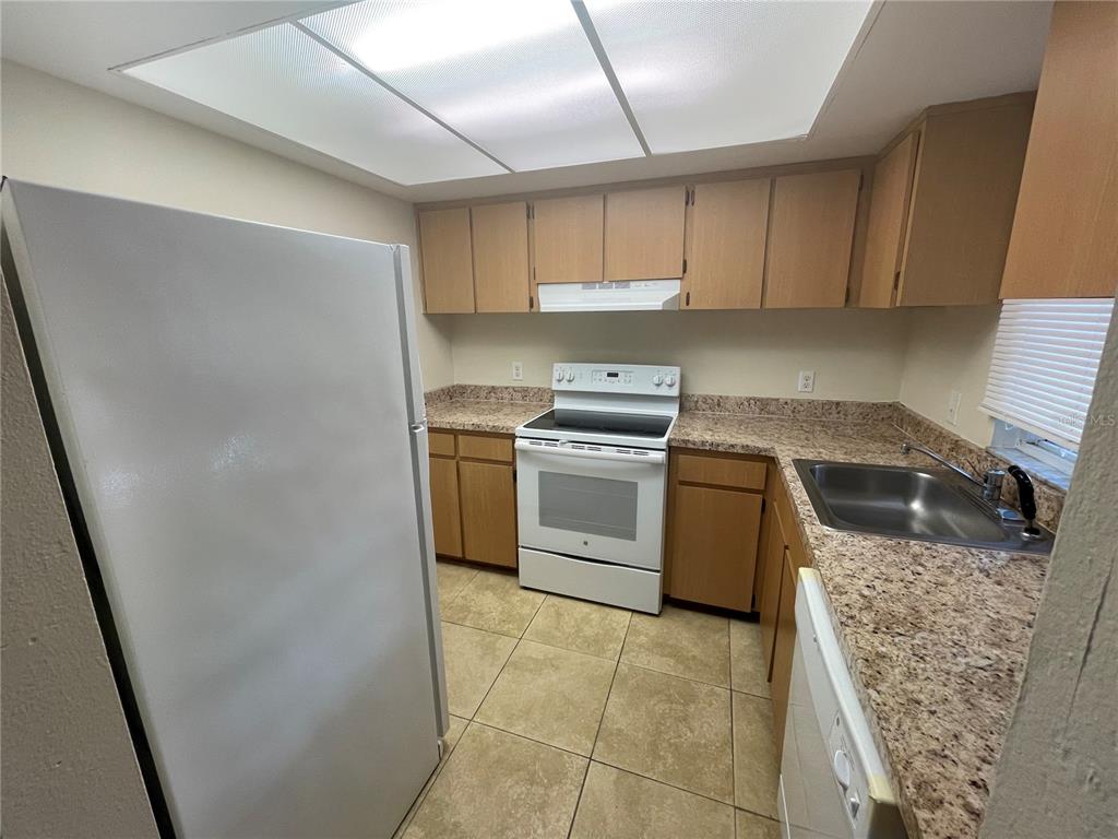 A kitchen features light wood cabinets, speckled laminate countertops, white appliances, and tiled flooring — 584 FAIRWAYS LANE UNIT F102, OCALA, FL