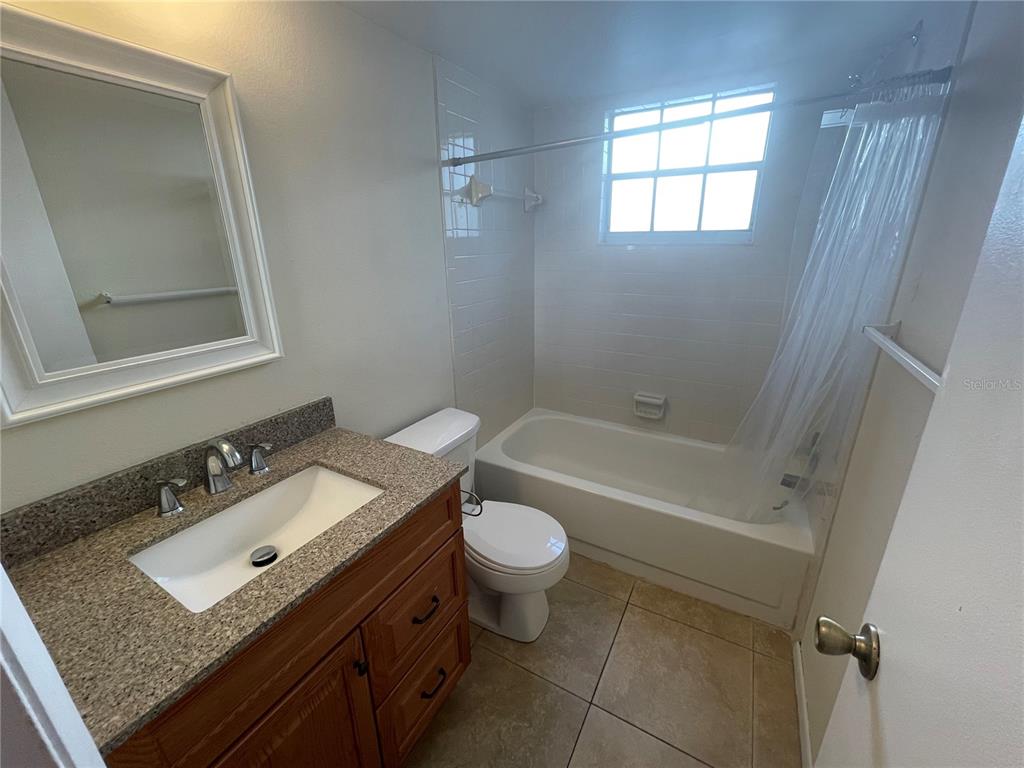 A bathroom featuring a wood vanity, granite countertop, toilet, and a shower-tub combination — 584 FAIRWAYS LANE UNIT F102, OCALA, FL