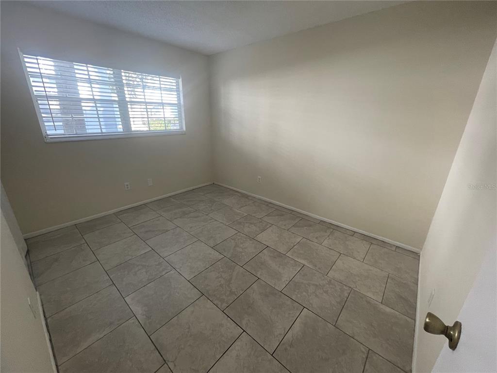 An empty room features light-colored walls, a window with blinds, and gray tiled flooring — 584 FAIRWAYS LANE UNIT F102, OCALA, FL