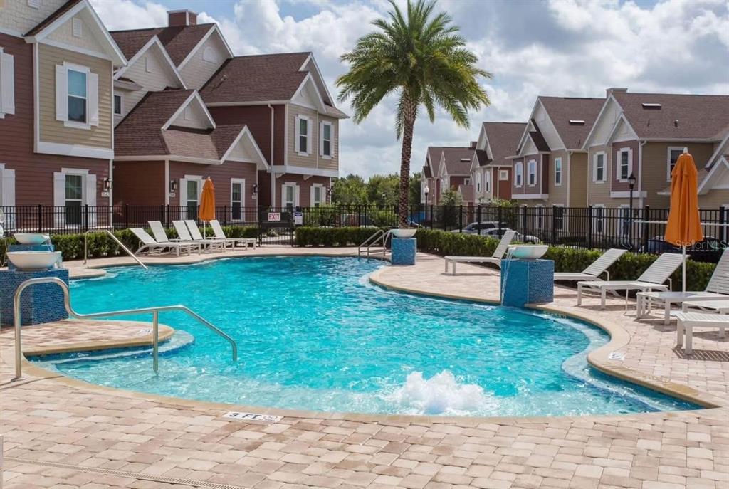 A swimming pool with lounge chairs and umbrellas sits in front of multi-story residential buildings — 7571 SUNNY DREAMS LANE UNIT na, KISSIMMEE, FL