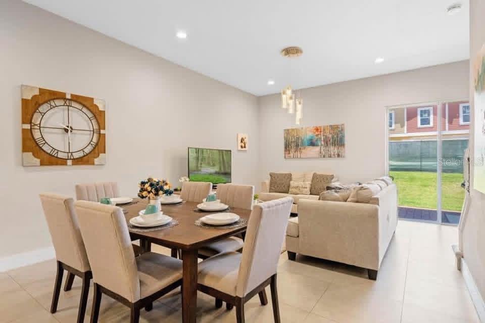 A dining area with a wooden table and chairs opens into a living room with tile floors — 7571 SUNNY DREAMS LANE UNIT na, KISSIMMEE, FL