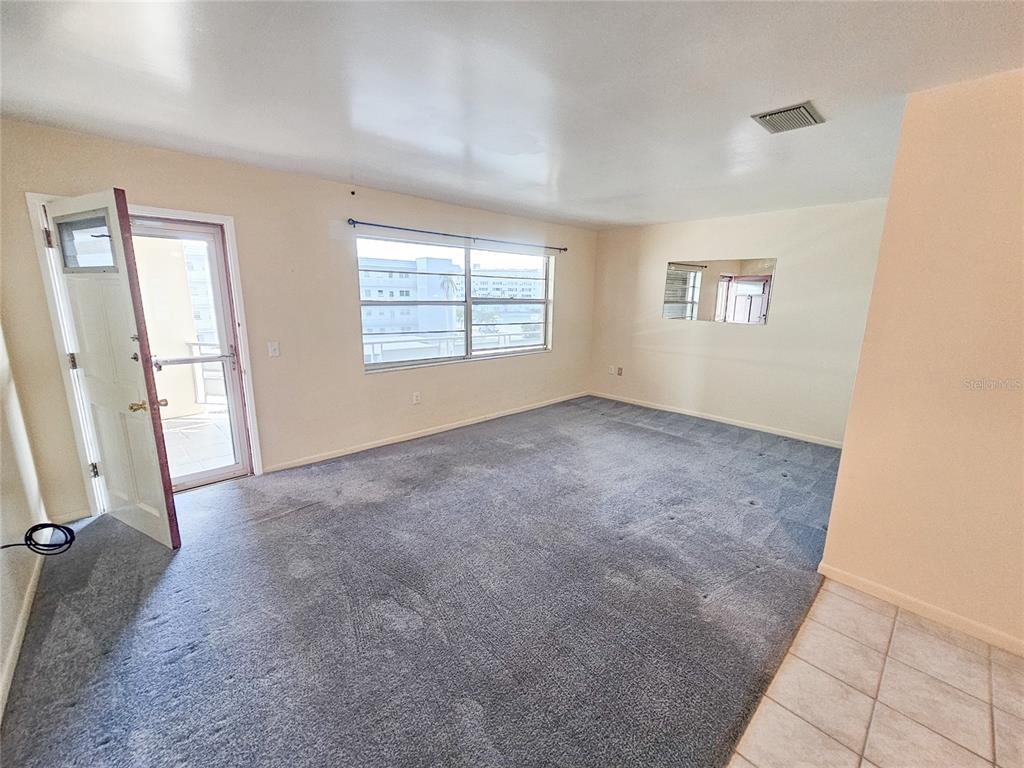 An empty living room features gray carpeting, beige walls, a large window, and a door — 3010 59TH STREET S UNIT 309, GULFPORT, FL