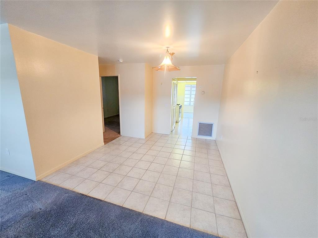 A dining area with light-colored tile flooring connects to a kitchen and a carpeted room — 3010 59TH STREET S UNIT 309, GULFPORT, FL