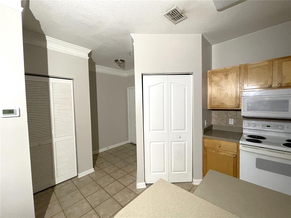 A kitchen features light-colored cabinets, white appliances, and tiled flooring leading to a hallway — 4207 S DALE MABRY HIGHWAY UNIT 9201, TAMPA, FL