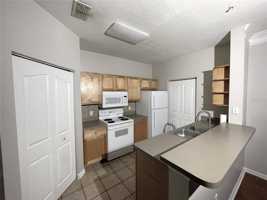 A kitchen features light wood cabinets, white appliances, a breakfast bar, and tile flooring — 4207 S DALE MABRY HIGHWAY UNIT 9201, TAMPA, FL