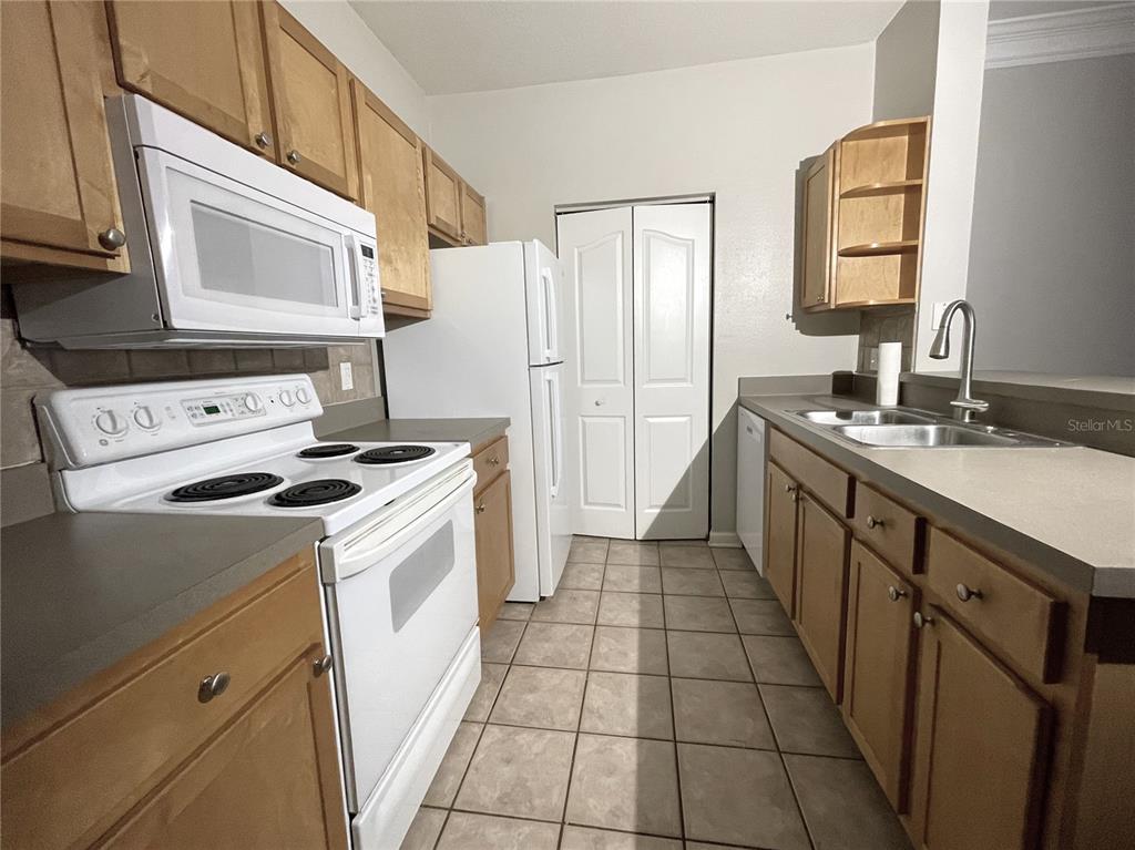 A galley-style kitchen features light wood cabinets, white appliances, and beige tile flooring — 4207 S DALE MABRY HIGHWAY UNIT 9201, TAMPA, FL
