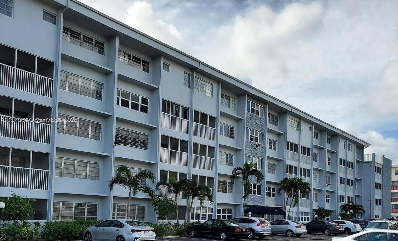 A multi-story apartment building with a light blue facade and a parking lot in front — 329 SE 3rd St # 305S, Hallandale Beach FL 33009, HALLANDALE BEACH, FL