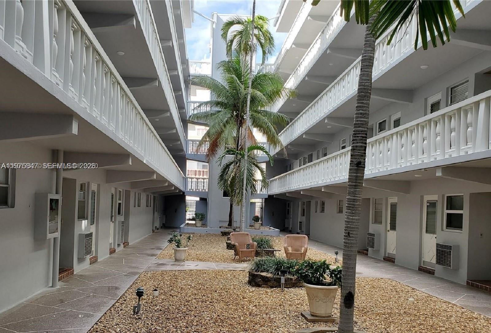 An outdoor courtyard features a gravel ground, palm trees, and two chairs between apartment buildings — 329 SE 3rd St # 305S, Hallandale Beach FL 33009, HALLANDALE BEACH, FL