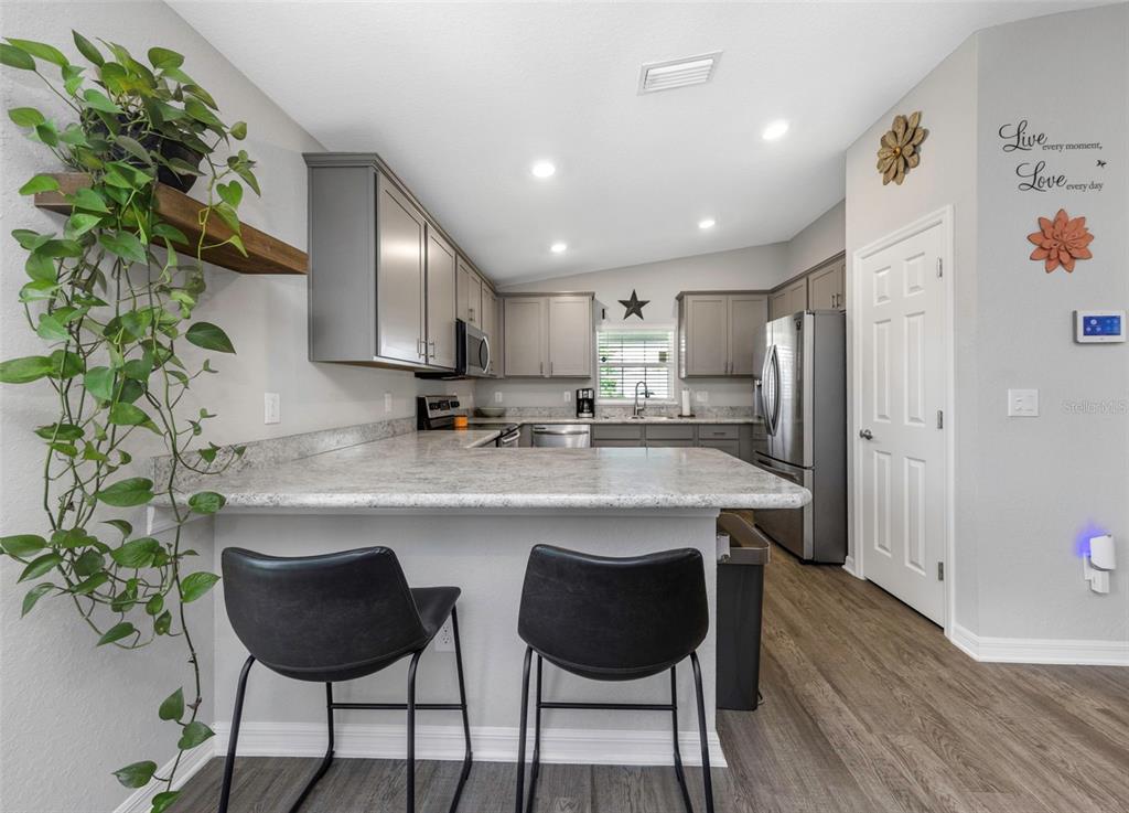 A kitchen features gray cabinets, a light-colored countertop, two bar stools, and a hanging plant — 3127 58TH WAY E, PALMETTO, FL