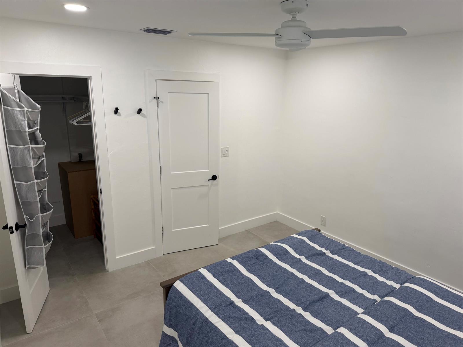 A bedroom with white walls, tile flooring, a ceiling fan, and an open closet door — 298 SW 6th Street # 2080, Boca Raton FL 33432, BOCA RATON, FL