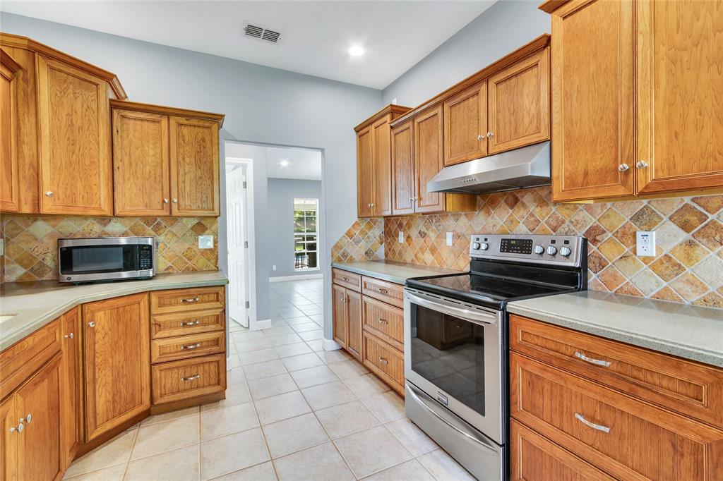 A kitchen features wood cabinets, a stainless steel stove, a microwave, and a tiled backsplash — 8206 SIMMONS STREET, BROOKSVILLE, FL