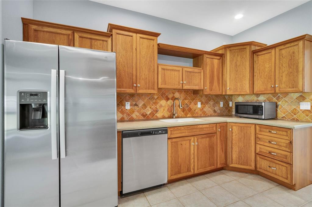 A kitchen features oak cabinets, stainless steel appliances, and a diagonal-patterned tile backsplash — 8206 SIMMONS STREET, BROOKSVILLE, FL