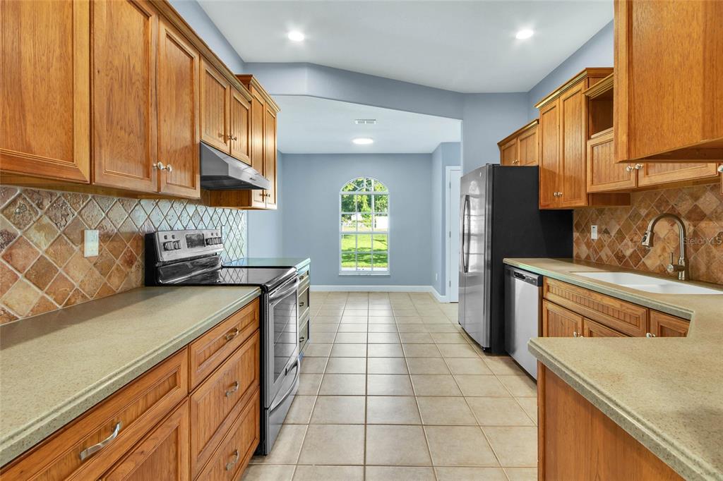 A kitchen features wood cabinets, tile backsplashes, stainless steel appliances, and a tiled floor — 8206 SIMMONS STREET, BROOKSVILLE, FL