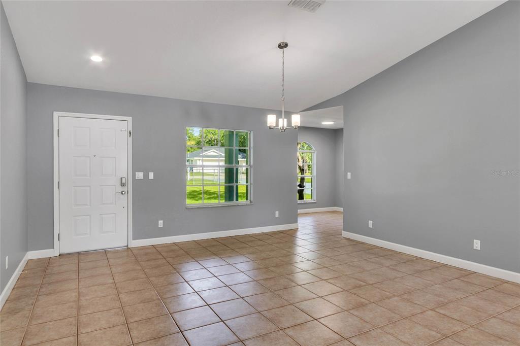An empty room with gray walls, tiled floors, a white front door, and a chandelier — 8206 SIMMONS STREET, BROOKSVILLE, FL
