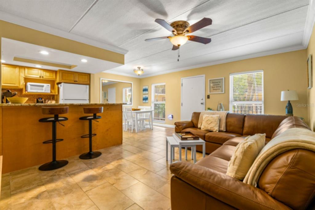 An open-concept living room and kitchen feature tile flooring, a leather sofa, and bar seating — 8911 BLIND PASS ROAD UNIT 223, ST PETE BEACH, FL