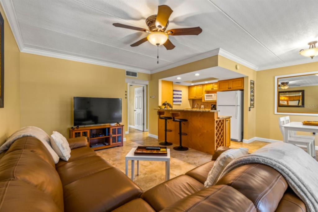 A living room with a brown leather sofa, television, and an open kitchen with bar seating — 8911 BLIND PASS ROAD UNIT 223, ST PETE BEACH, FL