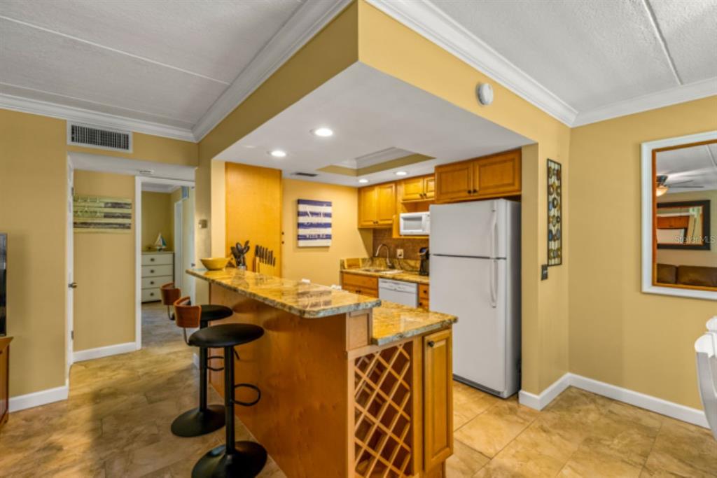 A kitchen with wood cabinets, granite countertops, a breakfast bar, and tile flooring — 8911 BLIND PASS ROAD UNIT 223, ST PETE BEACH, FL