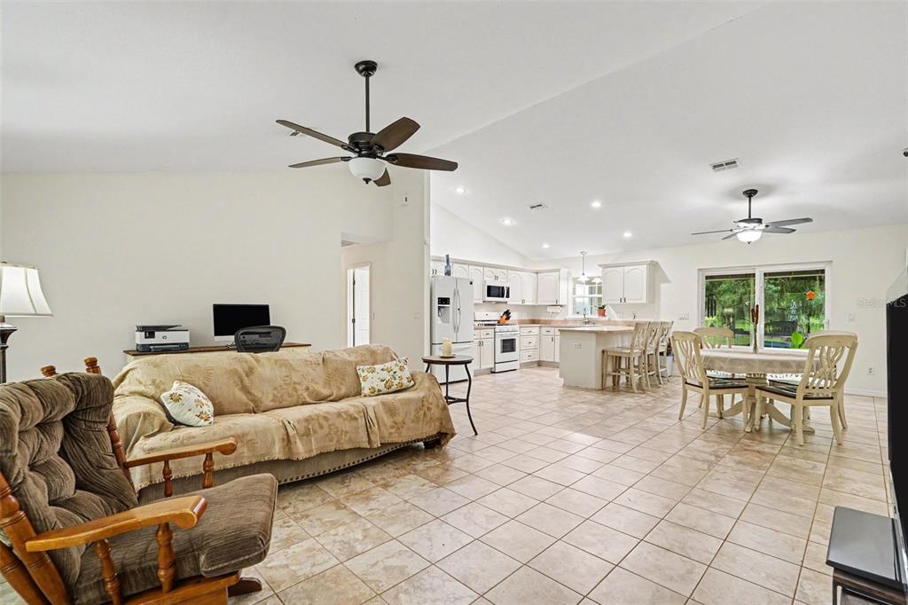 An open-concept living room, dining area, and kitchen with tile floors and vaulted ceilings — 7697 W C 476, BUSHNELL, FL
