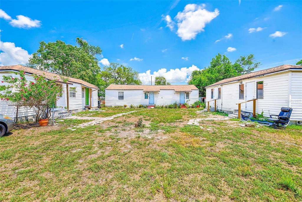Three white single-story buildings surround a grassy courtyard with stone walkways under a blue sky — 3257 57TH AVENUE N, ST PETERSBURG, FL