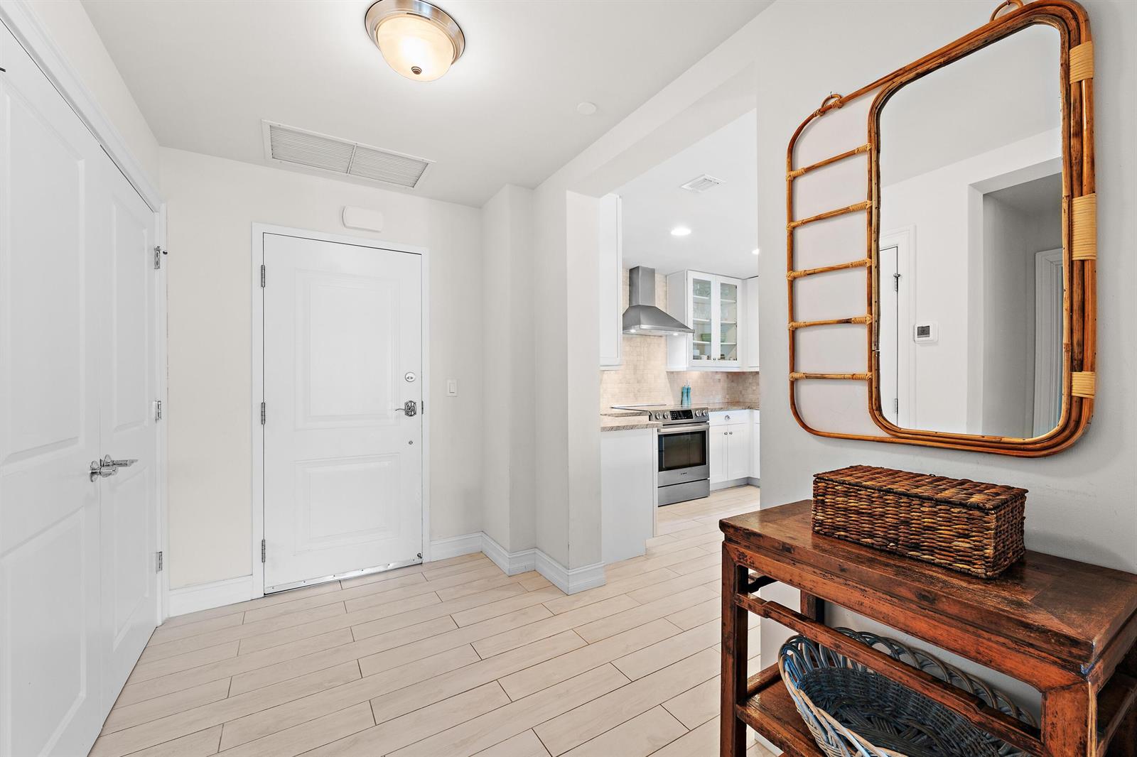 An entryway features light tile flooring, a wooden console table, and a view into the kitchen — 432 Bay Colony Drive N, Juno Beach FL 33408, JUNO BEACH, FL