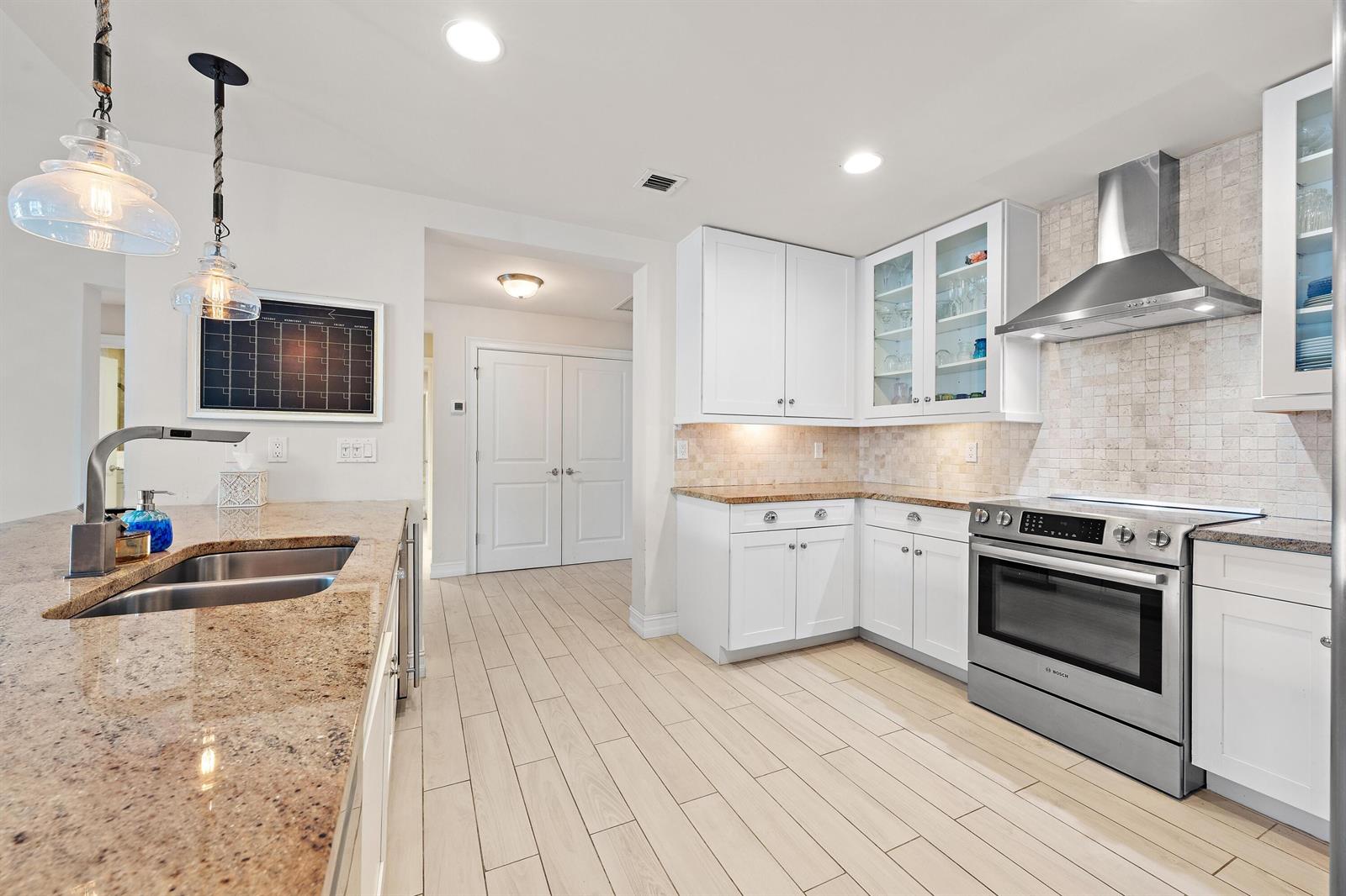 A kitchen with white cabinets, granite countertops, stainless steel appliances, and light-colored wood-look tile flooring — 432 Bay Colony Drive N, Juno Beach FL 33408, JUNO BEACH, FL