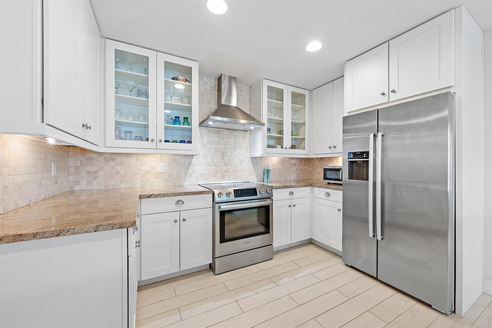 A kitchen features white cabinets, stainless steel appliances, granite countertops, and light-colored tile flooring — 432 Bay Colony Drive N, Juno Beach FL 33408, JUNO BEACH, FL