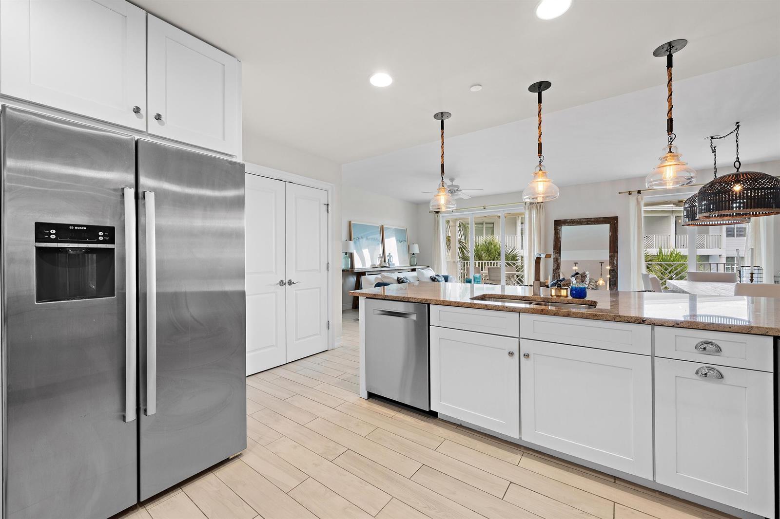 A kitchen with white cabinets, stainless steel appliances, a granite island, and light wood flooring — 432 Bay Colony Drive N, Juno Beach FL 33408, JUNO BEACH, FL