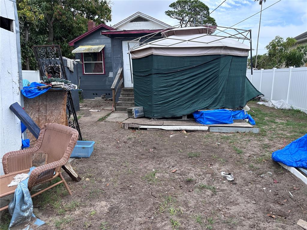 A backyard features a small house, a covered gazebo, a wicker chair, and scattered debris — 2389 HIGHWAY 73, MARIANNA, FL