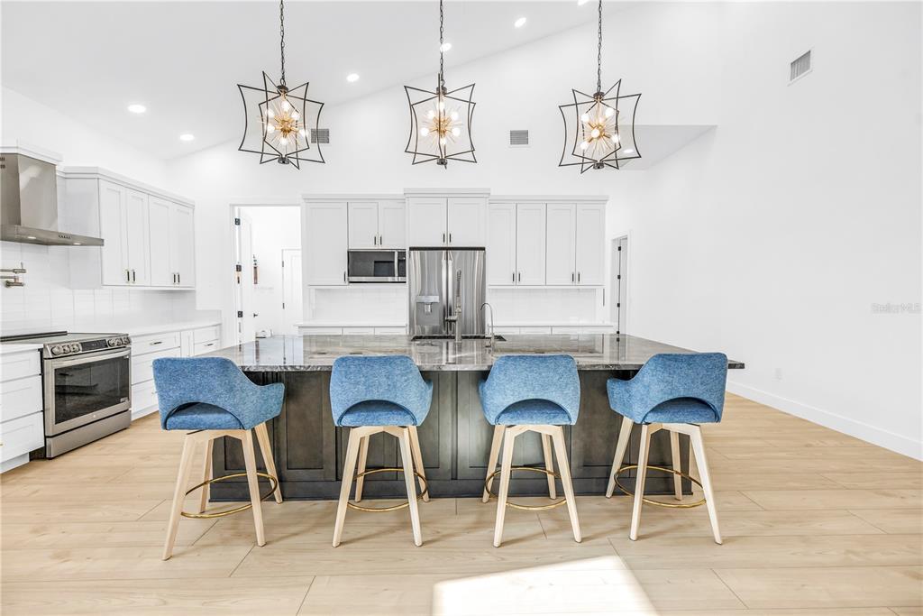 A modern kitchen features a large island with four blue stools under three pendant lights — 4907 15TH AVENUE N, ST PETERSBURG, FL