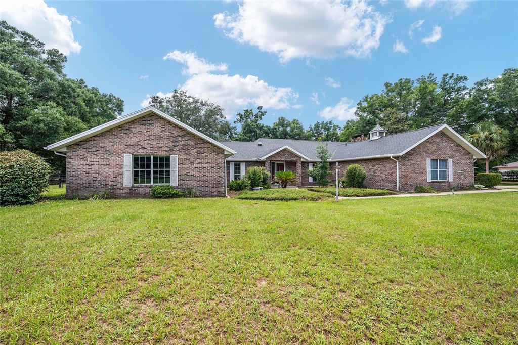 A single-story brick house with a large front lawn under a blue sky — 6968 SW 99TH STREET, OCALA, FL