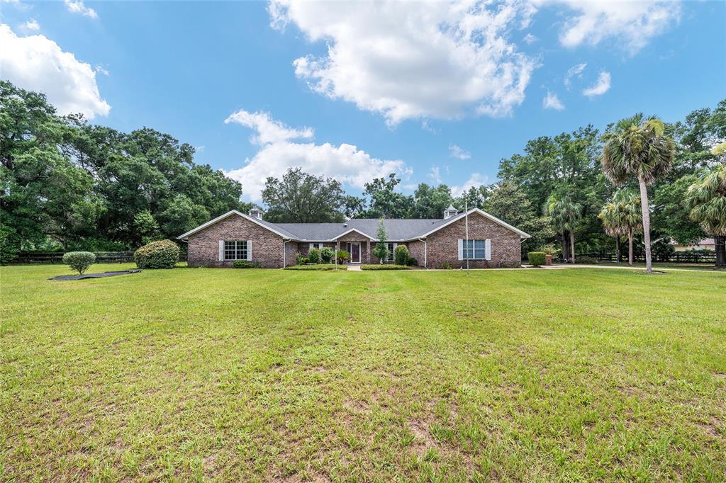 A single-story brick house with a dark roof sits on a large, grassy lawn — 6968 SW 99TH STREET, OCALA, FL