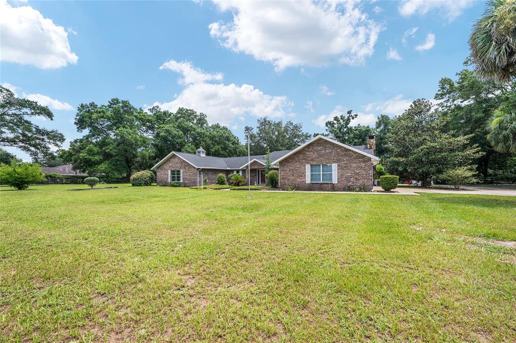 A single-story brick house with a large front lawn under a blue sky — 6968 SW 99TH STREET, OCALA, FL