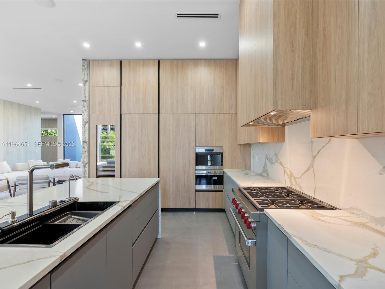 A modern kitchen features light wood cabinetry, a marble-topped island, and a stainless steel range — 871 NE 83rd St, Miami FL 33138, MIAMI, FL