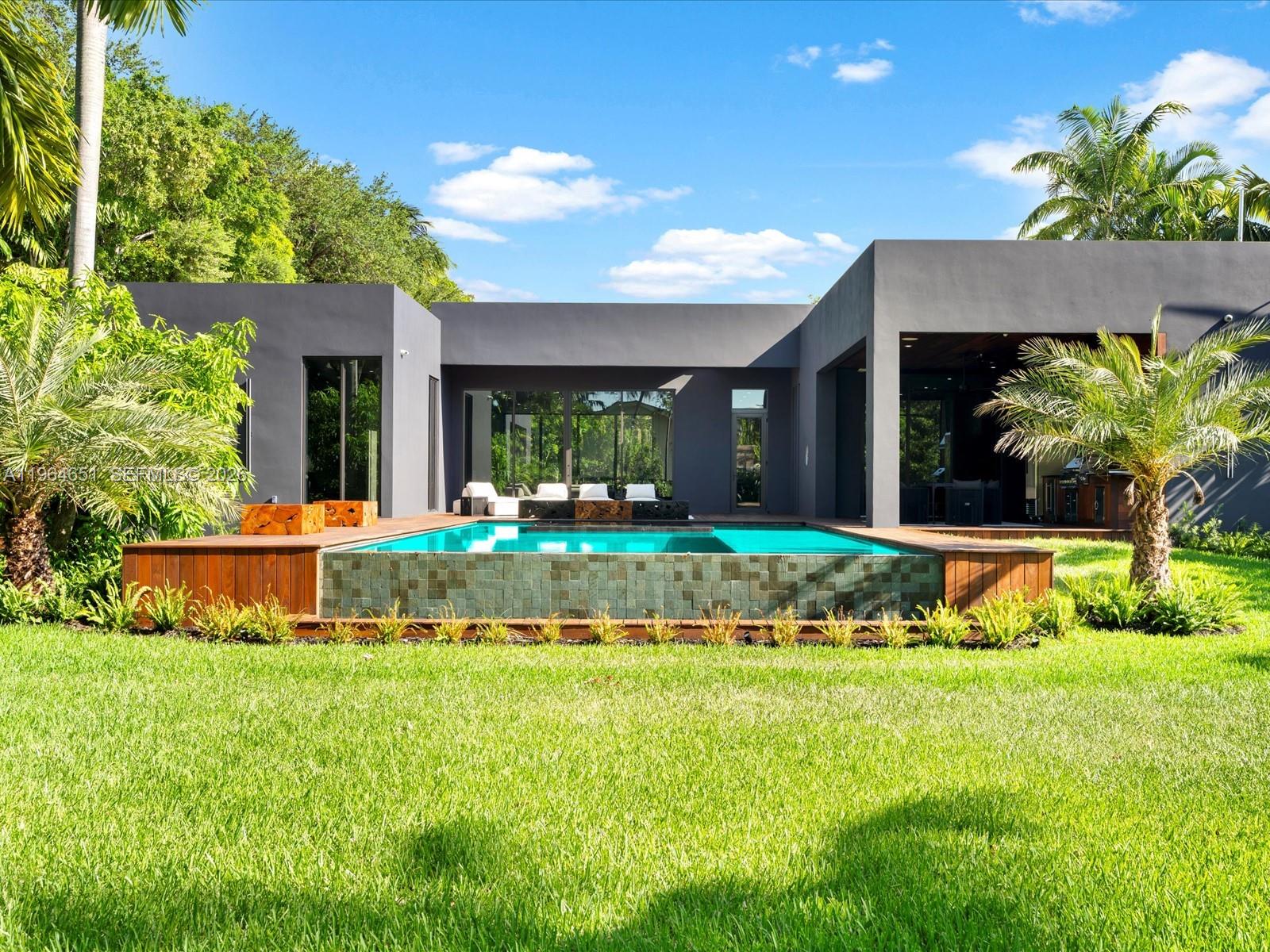 A modern gray house features a raised swimming pool with tiled sides and a wooden deck — 871 NE 83rd St, Miami FL 33138, MIAMI, FL