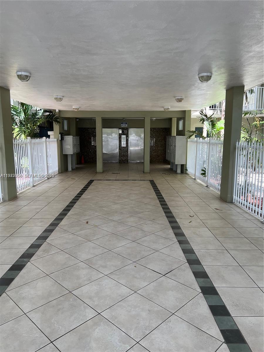 A covered outdoor entryway features tiled flooring, white fencing, and two elevator doors — 665 NE 83rd Ter # 112, Miami FL 33138, MIAMI, FL