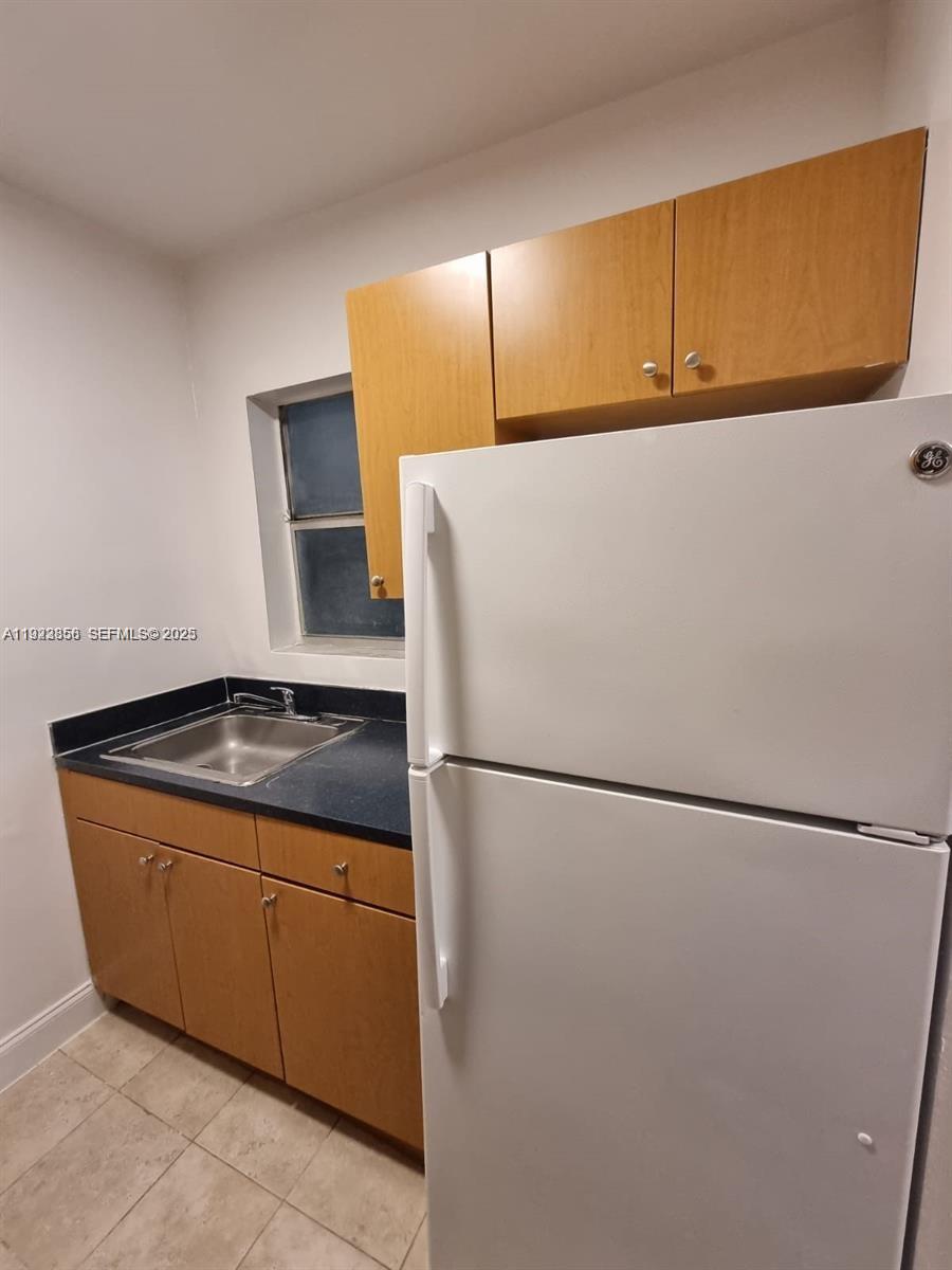 A small kitchen features light wood cabinets, a dark countertop, a sink, and a refrigerator — 665 NE 83rd Ter # 112, Miami FL 33138, MIAMI, FL