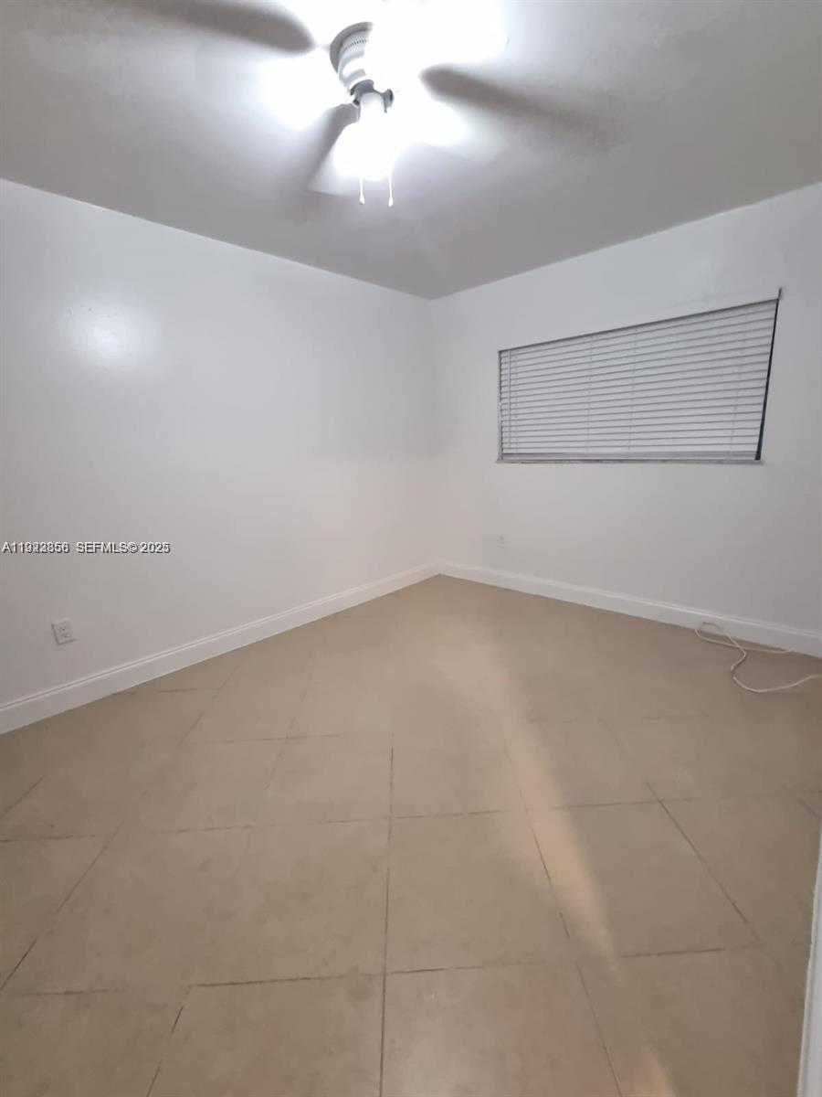 This empty bedroom features white walls, tile flooring, a ceiling fan, and a window — 665 NE 83rd Ter # 112, Miami FL 33138, MIAMI, FL