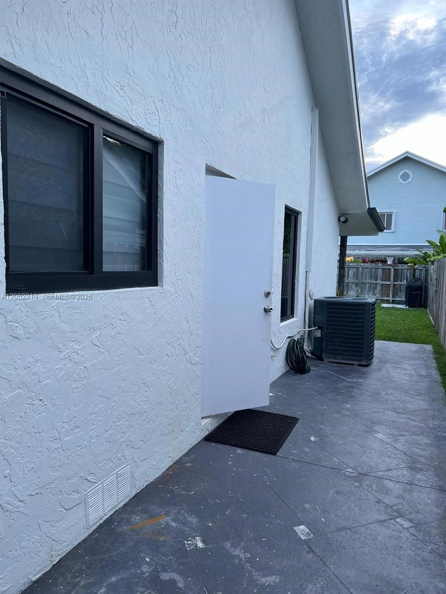 The exterior of a white stucco house features a door, windows, and an air conditioning unit — 10822 SW 142nd Ct # 1, Miami FL 33186, MIAMI, FL