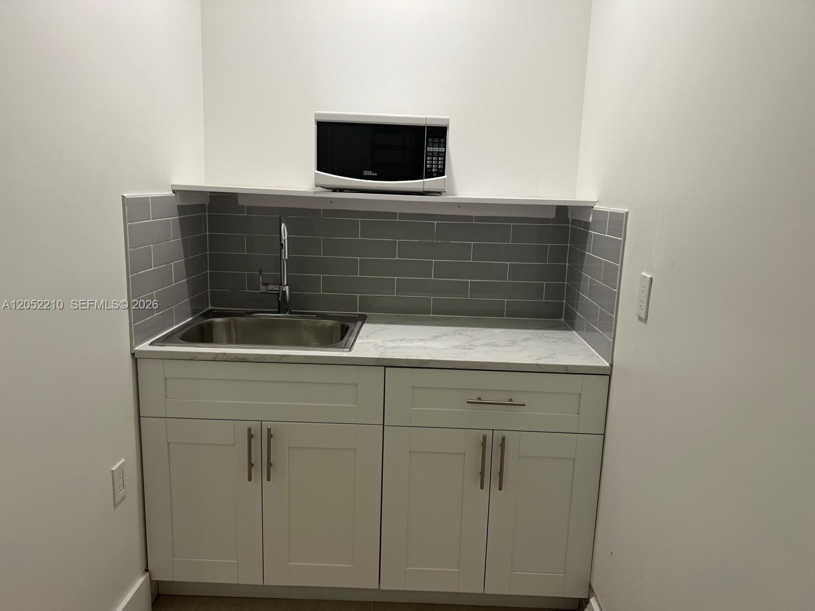 A small kitchenette features white cabinets, a marble-look countertop, a stainless steel sink, and a microwave — 10822 SW 142nd Ct # 1, Miami FL 33186, MIAMI, FL