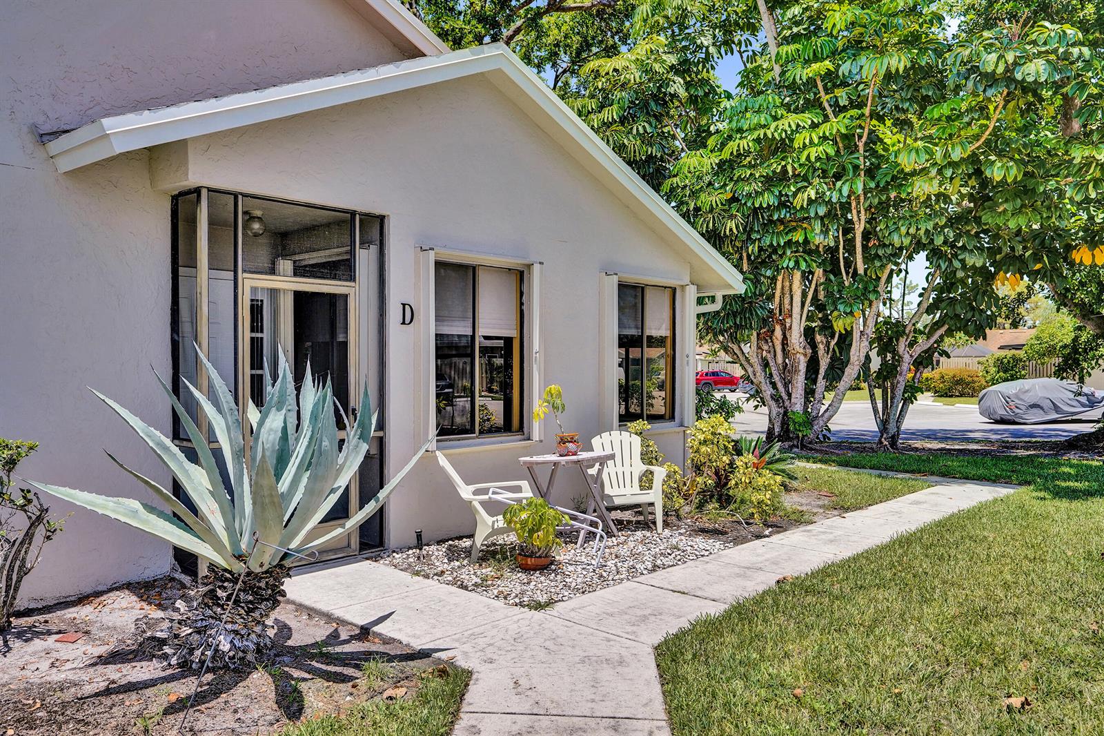 A light-colored exterior of a residential unit with a screened entrance, patio, and large agave — 2915 NW 12th Street # D, Delray Beach FL 33445, DELRAY BEACH, FL
