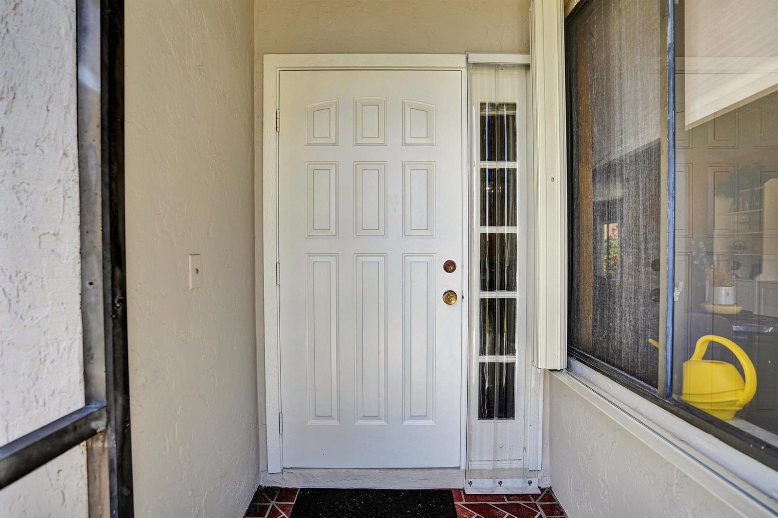 A white front door with a side window light sits on a tiled porch — 2915 NW 12th Street # D, Delray Beach FL 33445, DELRAY BEACH, FL