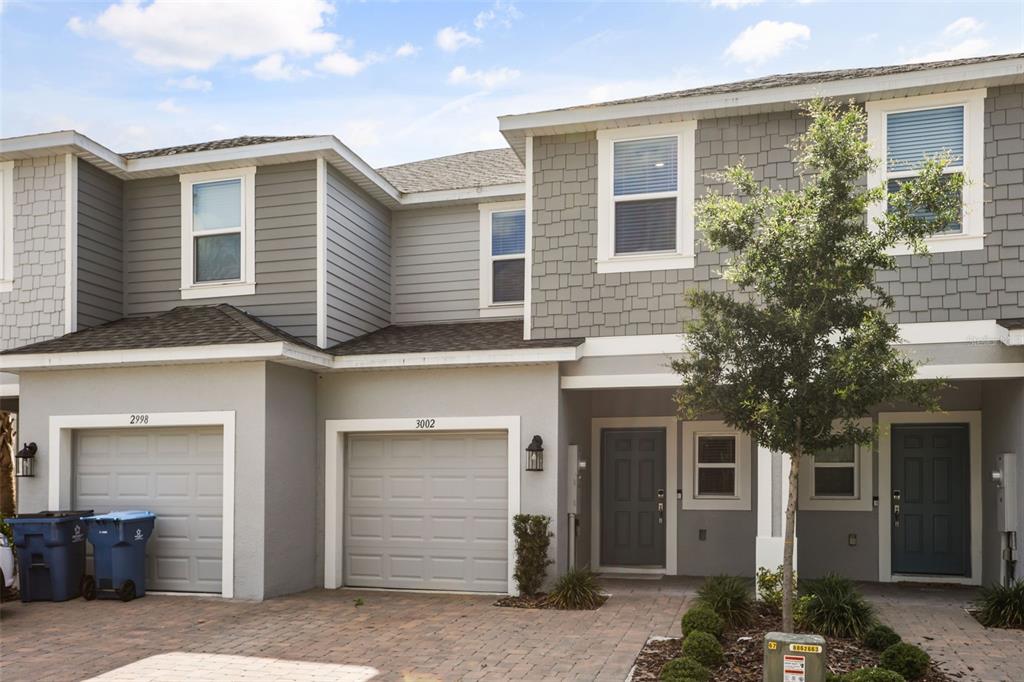 A two-story townhouse exterior with gray siding, two garage doors, and a paved driveway — 3002 CANARY AVENUE, DAVENPORT, FL