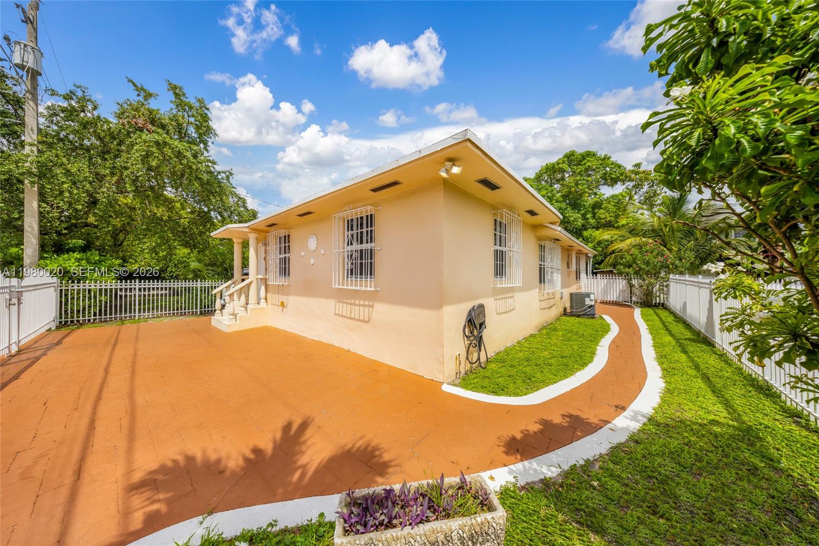 The exterior of a beige house features a paved patio, white fencing, and green lawn — 287 NW 31st St, Miami FL 33127, MIAMI, FL