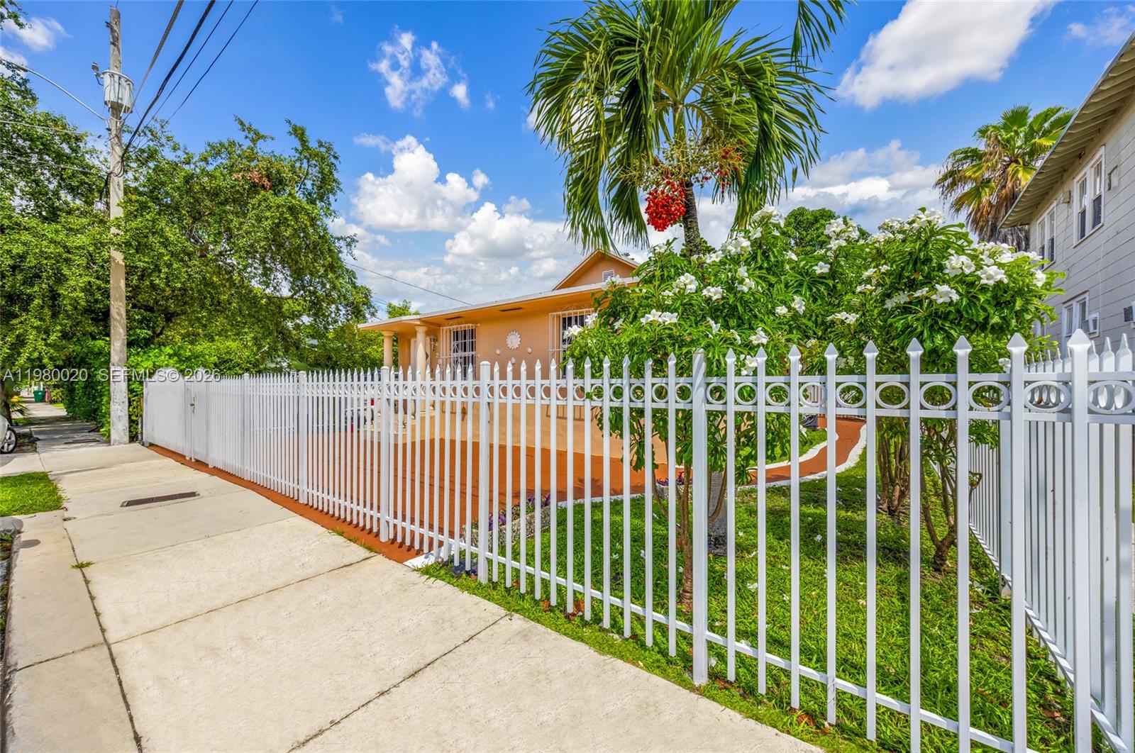 A white metal fence borders the sidewalk in front of a peach-colored house with landscaping — 287 NW 31st St, Miami FL 33127, MIAMI, FL