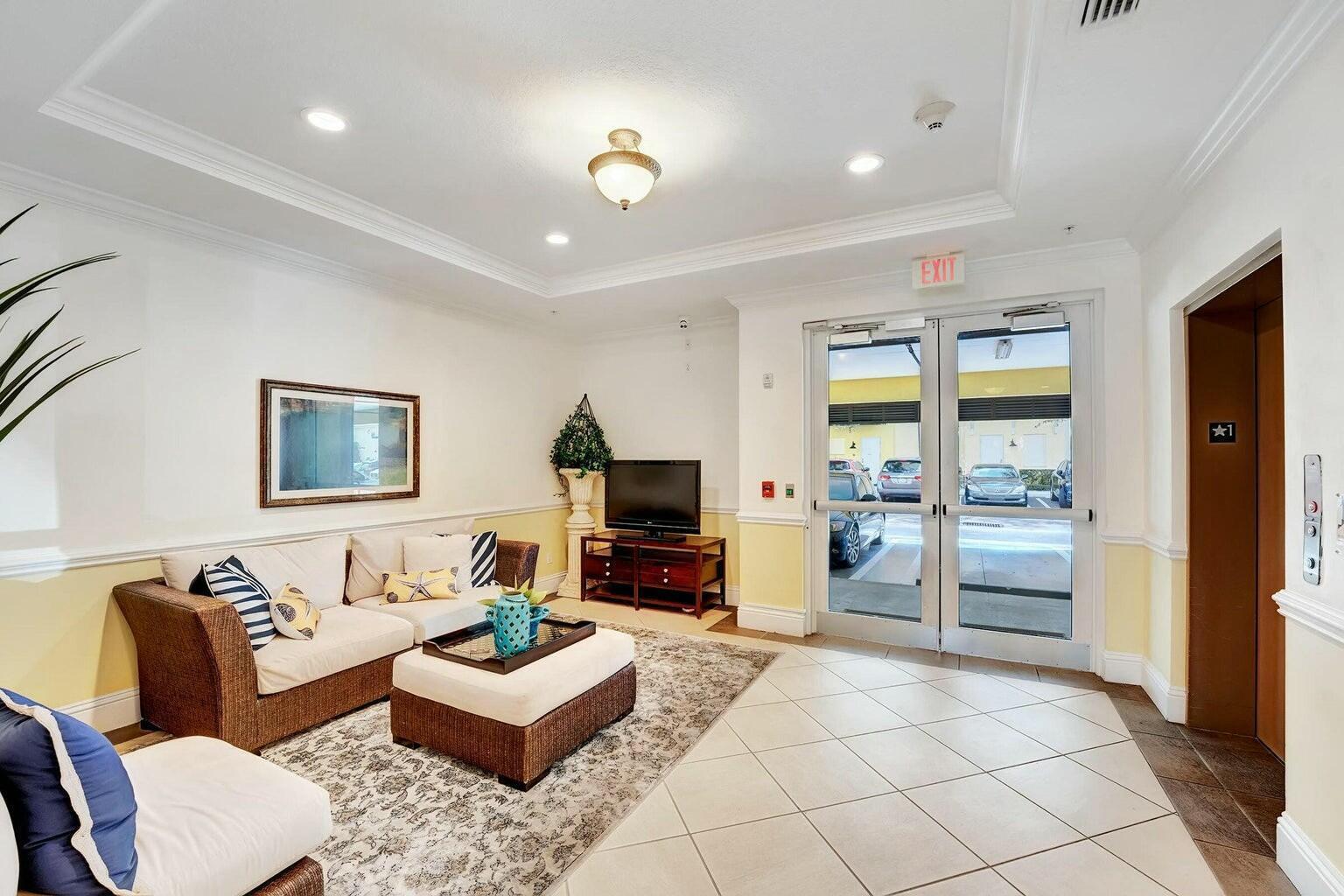 A furnished lobby area features a sofa, television, tiled floors, and glass exit doors — 3120 E Latitude Circle # 206, Delray Beach FL 33483, DELRAY BEACH, FL