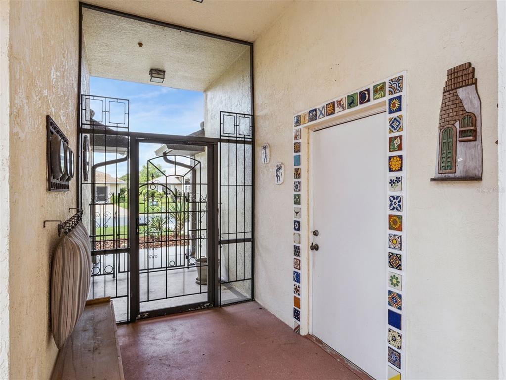 A covered entryway features a metal security gate, a white door with decorative tiles, and a bench — 21815 TARTAN STREET, LEESBURG, FL