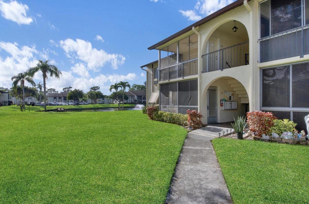 A two-story apartment building with screened balconies overlooks a grassy lawn and a pond — 3527 La Palmas Court # 1, FL 33463, FL