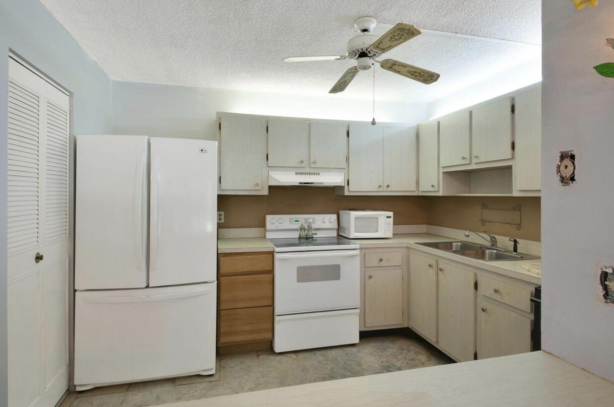 A kitchen features white appliances, light wood-toned cabinets, a ceiling fan, and a neutral backsplash — 3527 La Palmas Court # 1, FL 33463, FL