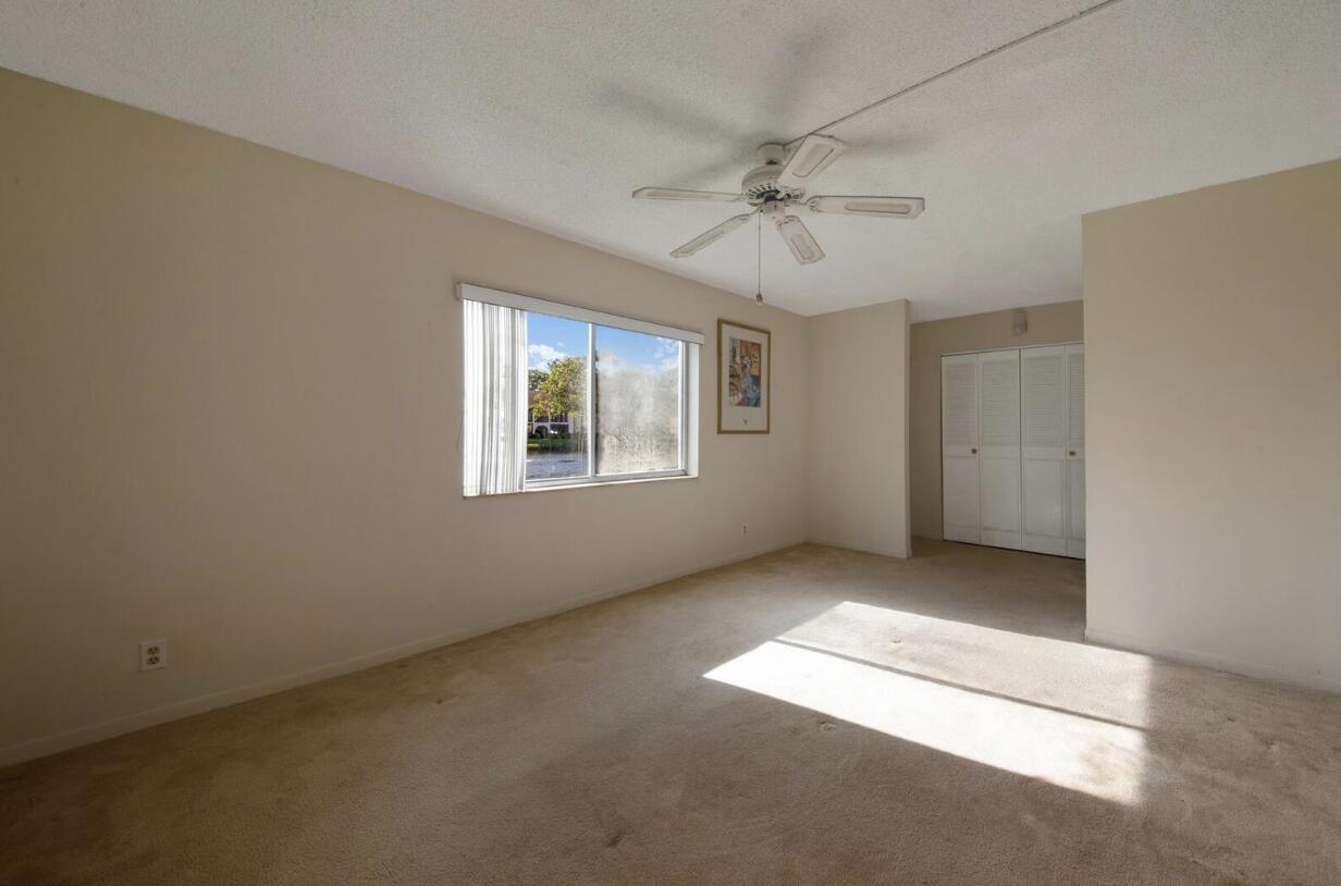 An empty bedroom with beige carpet, a ceiling fan, a window, and white closet doors — 3527 La Palmas Court # 1, FL 33463, FL